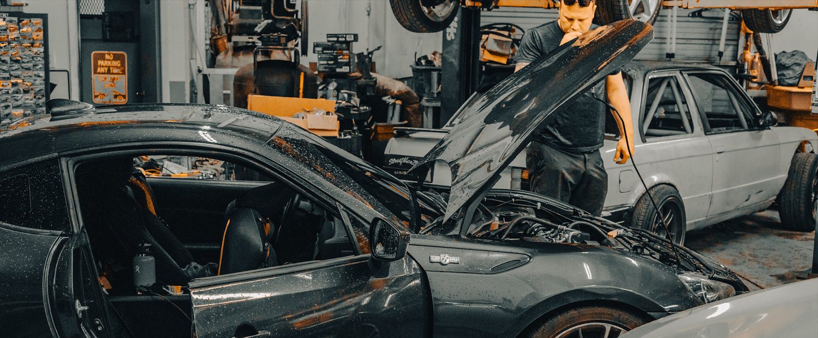 The floor at Car Buffet in Holly Hill, Florida, with someone leaning over the open engine bay of a dark coupe, a caged white sedan alongside, and a car up on a lift